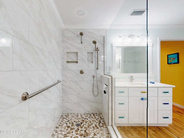 bathroom featuring tiled shower, ornamental molding, vanity, a textured ceiling, and hardwood / wood-style floors