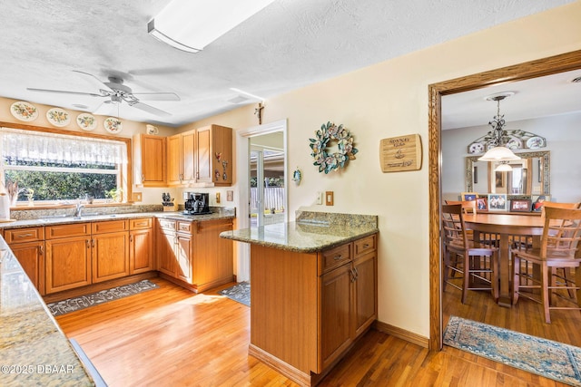 kitchen with sink, a textured ceiling, light wood-type flooring, kitchen peninsula, and pendant lighting