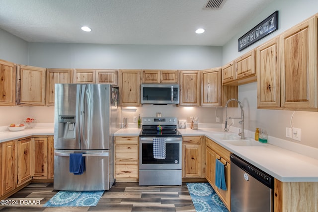 kitchen with appliances with stainless steel finishes, a textured ceiling, dark hardwood / wood-style floors, light brown cabinets, and sink