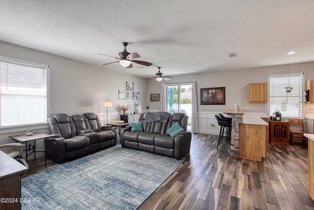 living room featuring ceiling fan, a textured ceiling, and dark hardwood / wood-style floors