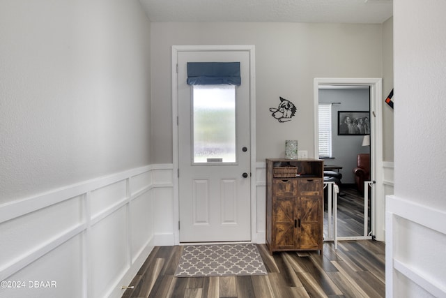 doorway with a wainscoted wall, dark wood finished floors, and a decorative wall