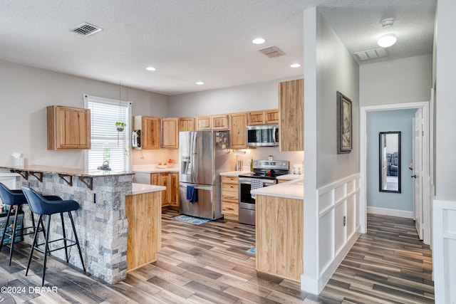 kitchen with kitchen peninsula, appliances with stainless steel finishes, wood-type flooring, and a breakfast bar