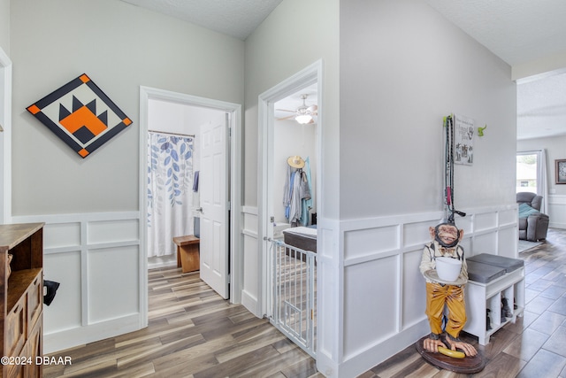 hallway featuring light wood-type flooring, wainscoting, a decorative wall, and a textured ceiling