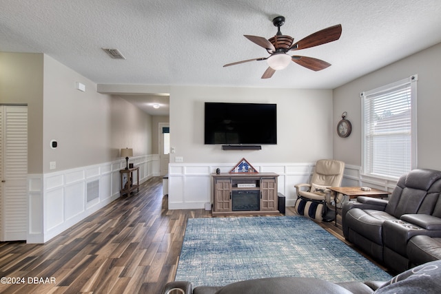 living room with a ceiling fan, a fireplace, visible vents, and dark wood-style flooring