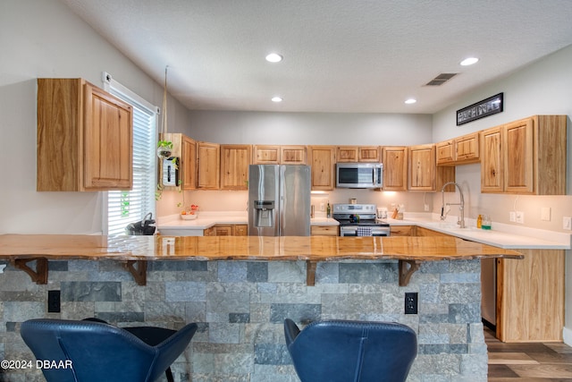 kitchen with stainless steel appliances, a textured ceiling, dark hardwood / wood-style floors, a breakfast bar area, and kitchen peninsula