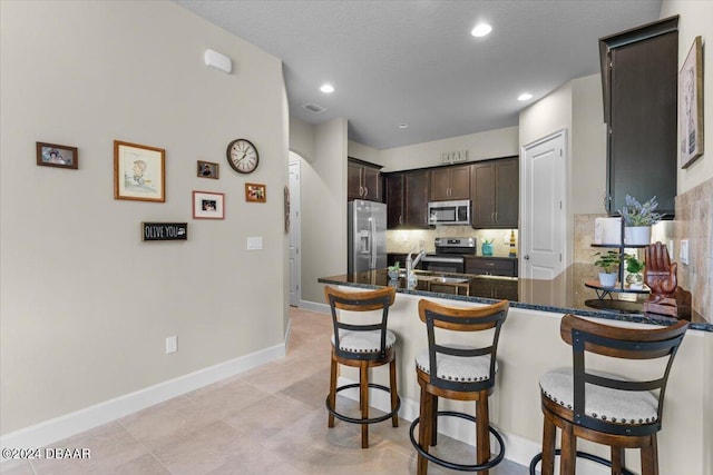 kitchen featuring kitchen peninsula, tasteful backsplash, appliances with stainless steel finishes, dark brown cabinets, and sink