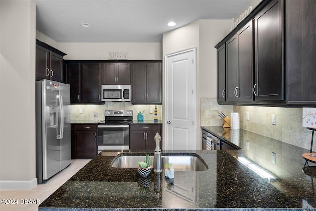 kitchen with stainless steel appliances, tasteful backsplash, dark stone counters, light tile patterned flooring, and sink