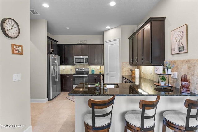 kitchen with dark stone countertops, stainless steel appliances, kitchen peninsula, light tile patterned floors, and sink