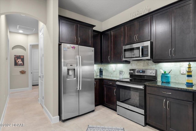 kitchen featuring appliances with stainless steel finishes, dark brown cabinets, dark stone countertops, and light tile patterned flooring