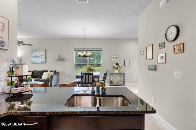 kitchen with sink, ceiling fan with notable chandelier, dark stone counters, dark brown cabinetry, and pendant lighting