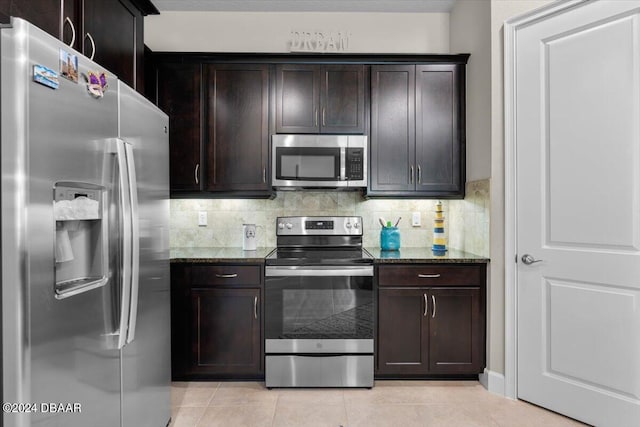 kitchen featuring light tile patterned flooring, dark brown cabinets, dark stone counters, and appliances with stainless steel finishes