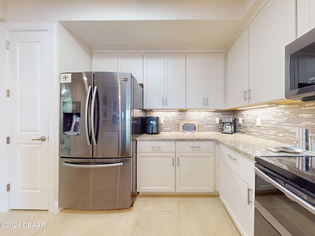 kitchen featuring light tile patterned flooring, white cabinetry, appliances with stainless steel finishes, backsplash, and light stone countertops