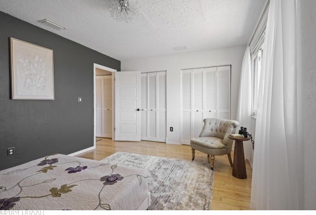 bedroom featuring light hardwood / wood-style floors, a textured ceiling, and multiple closets