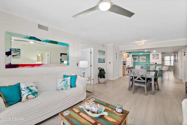 living room featuring wood finished floors, ornamental molding, visible vents, ceiling fan, and baseboards