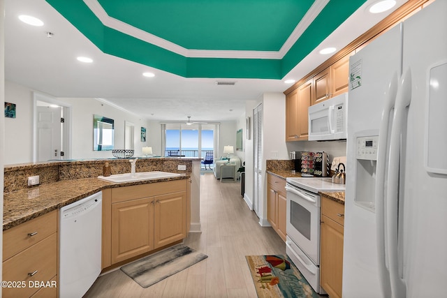 kitchen featuring light brown cabinetry, a tray ceiling, a sink, visible vents, and white appliances