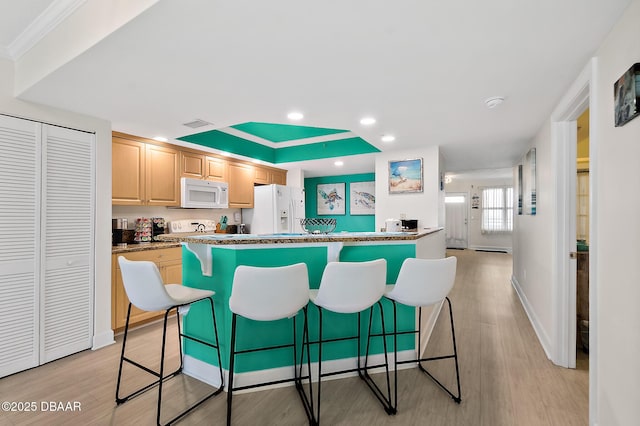 kitchen with a breakfast bar, white appliances, light brown cabinetry, and light wood-style floors