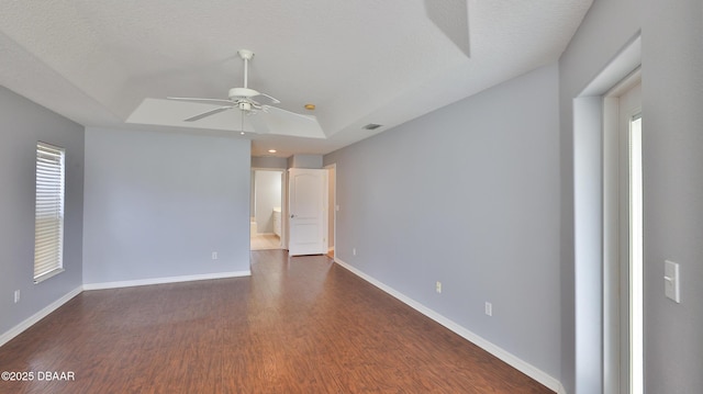 unfurnished room featuring a healthy amount of sunlight, dark hardwood / wood-style floors, ceiling fan, and a tray ceiling