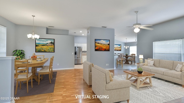 living room with ceiling fan with notable chandelier, vaulted ceiling, and light wood-type flooring