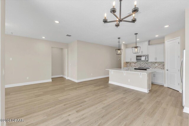 3116 Legends Preserve Dr, Daytona Beach, FL 32124 - kitchen with stainless steel microwave, a chandelier, decorative backsplash, light wood finished floors, and white cabinetry