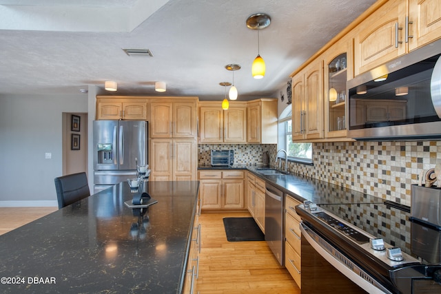 kitchen with decorative backsplash, appliances with stainless steel finishes, sink, pendant lighting, and light hardwood / wood-style floors