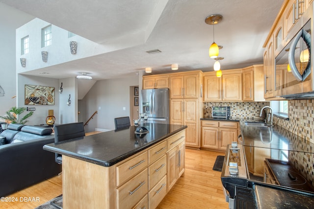 kitchen featuring light brown cabinets, hanging light fixtures, sink, appliances with stainless steel finishes, and a kitchen island