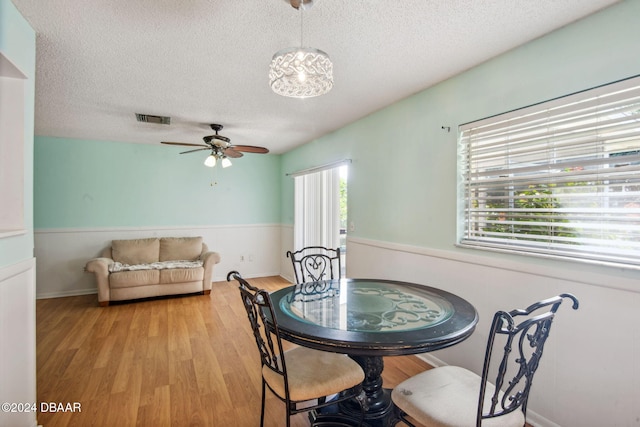 dining room featuring ceiling fan with notable chandelier, a textured ceiling, and light wood-type flooring