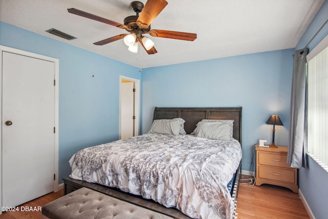 bedroom with a textured ceiling, multiple windows, light hardwood / wood-style flooring, and ceiling fan