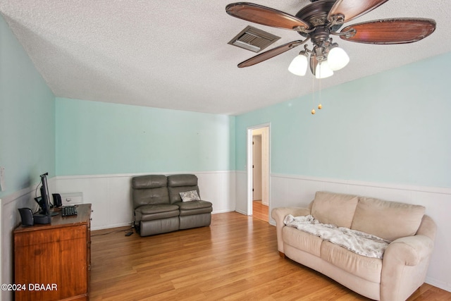 living room with ceiling fan, a textured ceiling, and light hardwood / wood-style floors