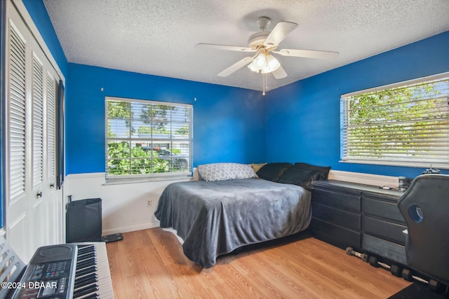 bedroom featuring a textured ceiling, light wood-type flooring, ceiling fan, and a closet