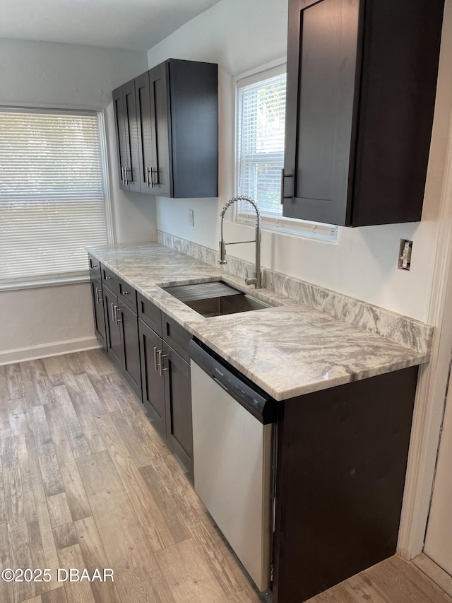 kitchen featuring baseboards, light wood-style flooring, light stone counters, stainless steel dishwasher, and a sink