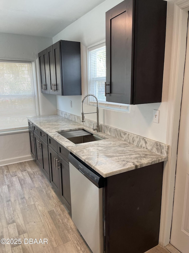 kitchen featuring baseboards, light stone countertops, stainless steel dishwasher, light wood-style floors, and a sink