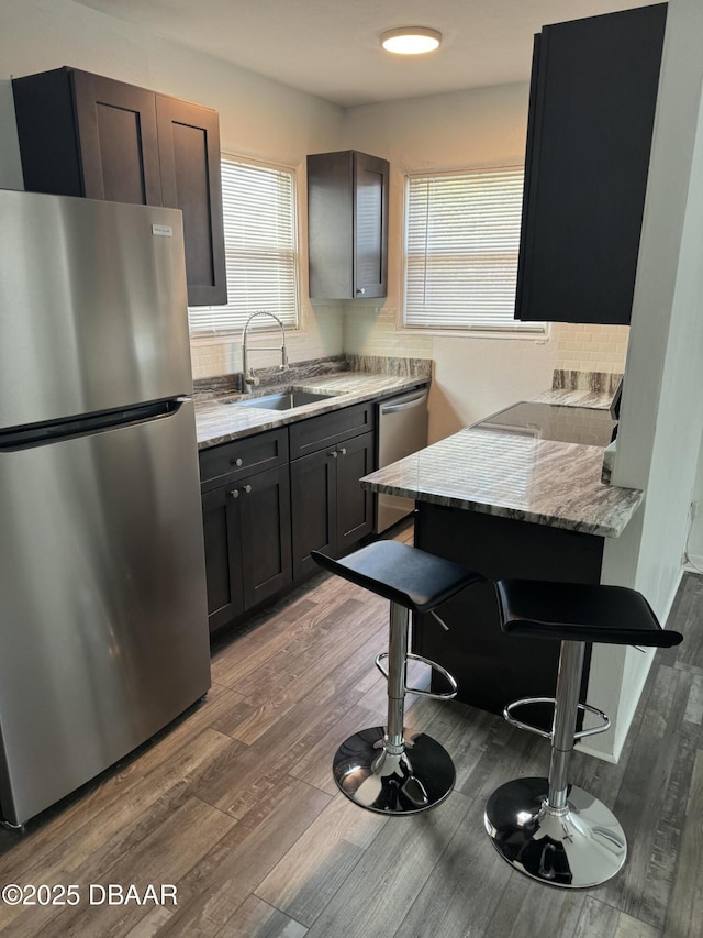 kitchen with a kitchen breakfast bar, dark wood-type flooring, light stone countertops, stainless steel appliances, and a sink