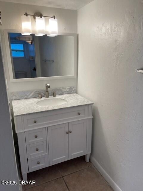 bathroom featuring a textured wall, tile patterned flooring, baseboards, and vanity