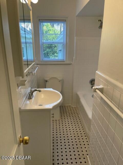 bathroom featuring toilet, vanity, tile walls, and wainscoting