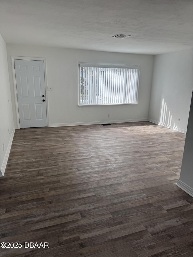 spare room with baseboards, visible vents, and dark wood finished floors