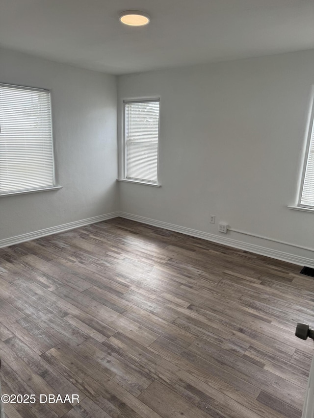 empty room featuring dark wood-style floors, visible vents, and baseboards