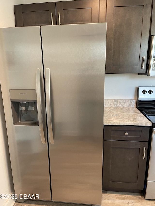 kitchen with appliances with stainless steel finishes, light stone counters, and dark brown cabinets