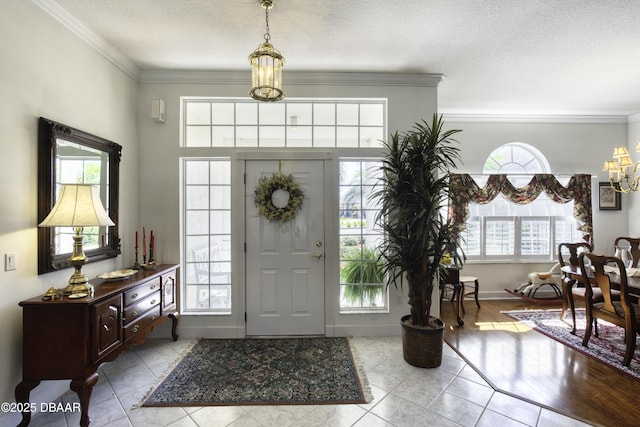 tiled foyer entrance featuring a textured ceiling, crown molding, baseboards, and a chandelier