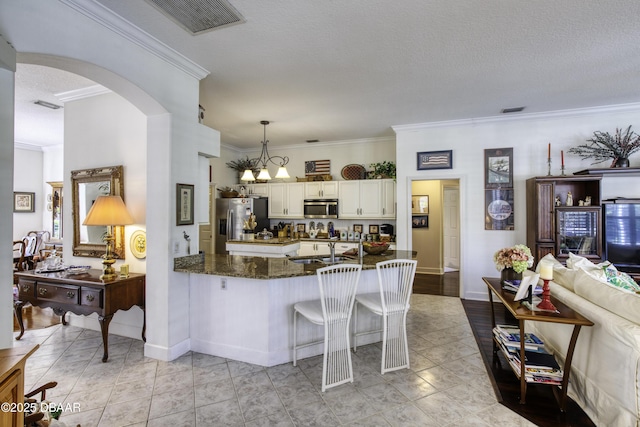 kitchen featuring pendant lighting, a sink, dark stone counters, arched walkways, and appliances with stainless steel finishes