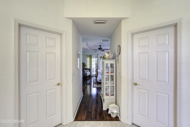 hallway featuring visible vents, baseboards, and wood finished floors