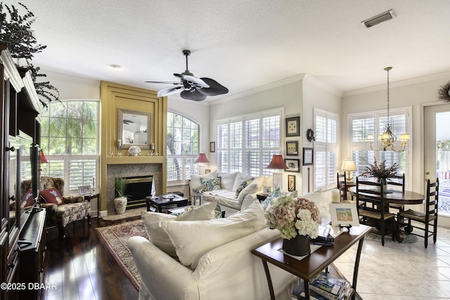 living area with visible vents, ornamental molding, ceiling fan with notable chandelier, a fireplace, and a textured ceiling