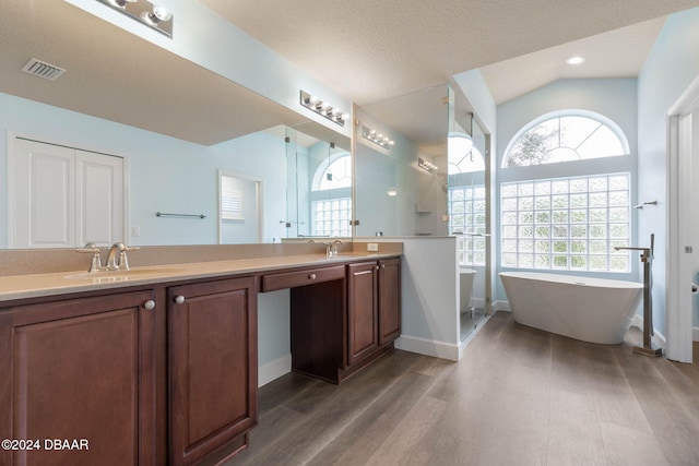 bathroom featuring a bathtub, vanity, vaulted ceiling, hardwood / wood-style flooring, and a textured ceiling