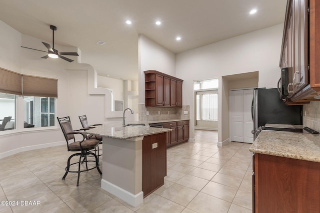 kitchen featuring a breakfast bar area, kitchen peninsula, light stone counters, and plenty of natural light