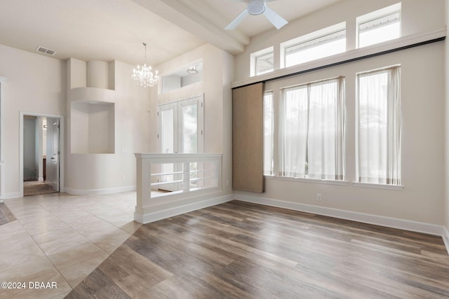 spare room featuring wood-type flooring, ceiling fan with notable chandelier, and a high ceiling