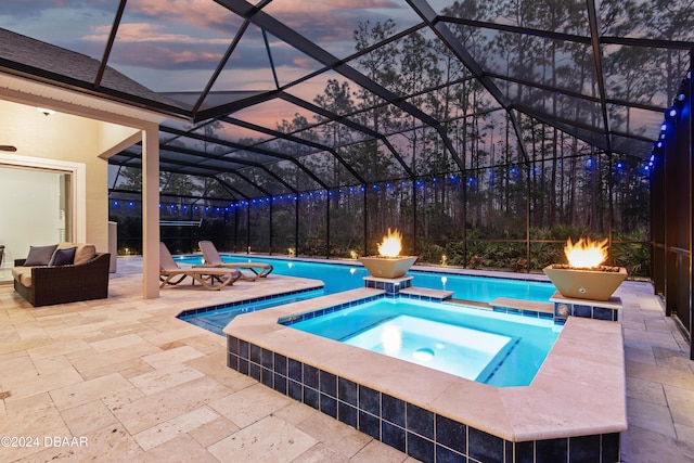 pool at dusk featuring glass enclosure, an in ground hot tub, and a patio area