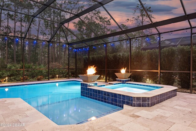 pool at dusk with an in ground hot tub, a patio area, and a lanai