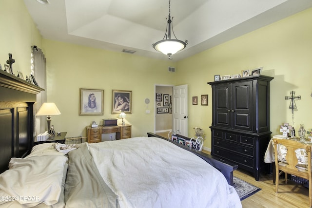 bedroom with a tray ceiling and light wood-type flooring