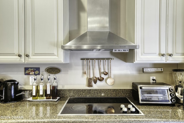 kitchen with black electric stovetop, white cabinets, and wall chimney range hood