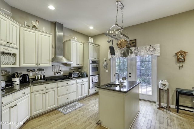 kitchen with french doors, light wood-type flooring, wall chimney exhaust hood, sink, and a center island with sink