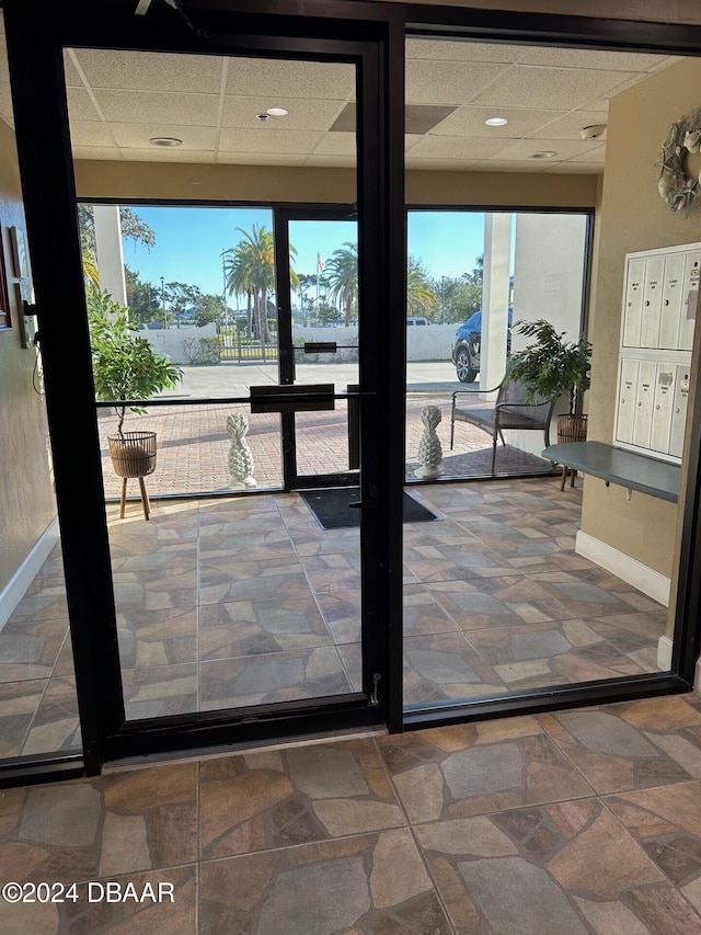 doorway to outside with a paneled ceiling, mail boxes, and a wealth of natural light